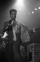 A black-haired man in a suit and tie performing onstage